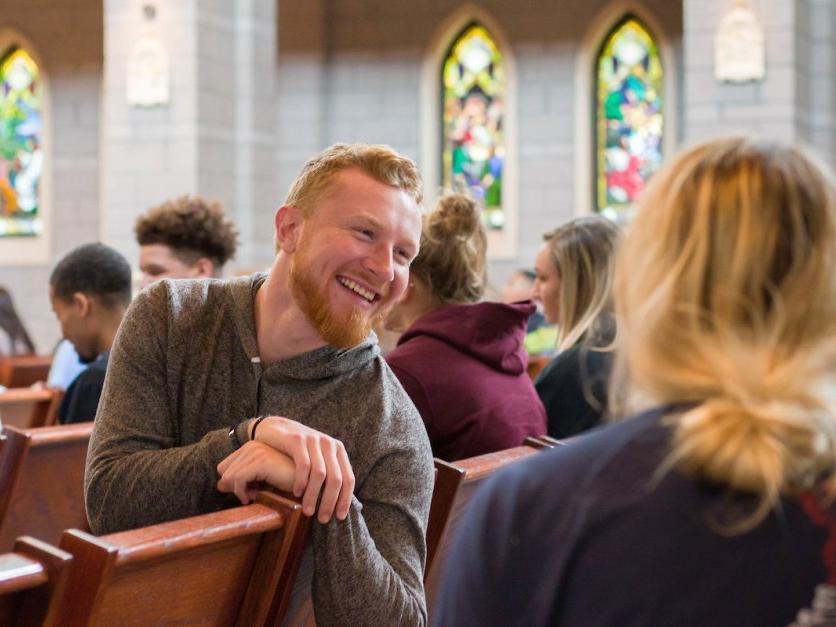 A student looks back at other while talking and smiling in chapel. 
